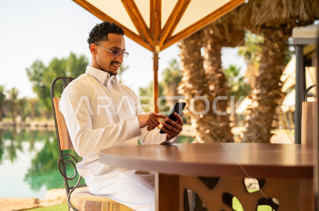 رجل سعودي بالثوب التقليدي يستخدم الهاتف الذكي في الخارج