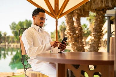 رجل سعودي بالثوب التقليدي يستخدم الهاتف الذكي في الخارج