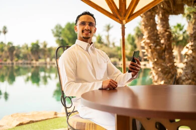 رجل سعودي بالثوب يستخدم الهاتف بجانب البحيرة