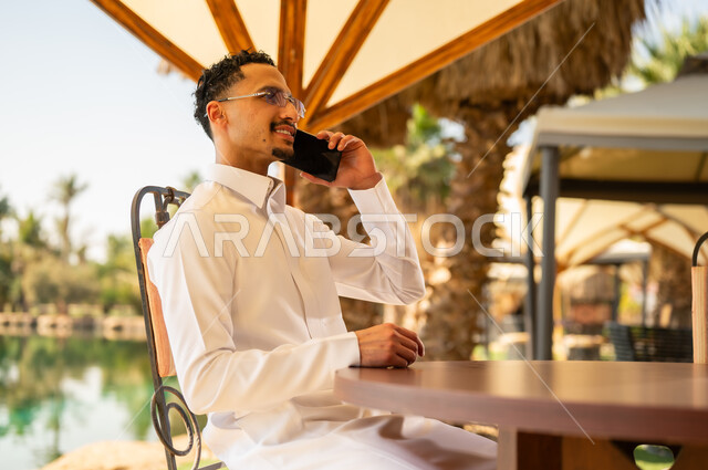 رجل سعودي بالثوب يتحدث بالهاتف في مكان خارجي