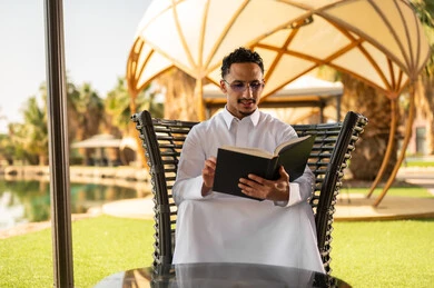 Saudi Man in White Thobe Reading Book Outdoors