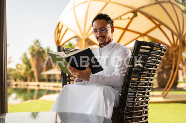 رجل سعودي يقرأ كتاباً في حديقة خارجية