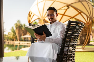 رجل سعودي يقرأ كتاباً في حديقة خارجية