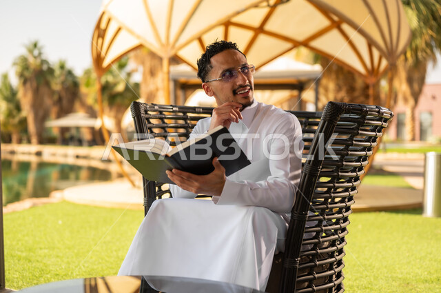 Saudi Man in Traditional Thobe Reading Book Outdoors