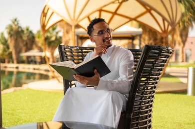رجل سعودي بالثوب التقليدي يقرأ كتاباً في الهواء الطلق