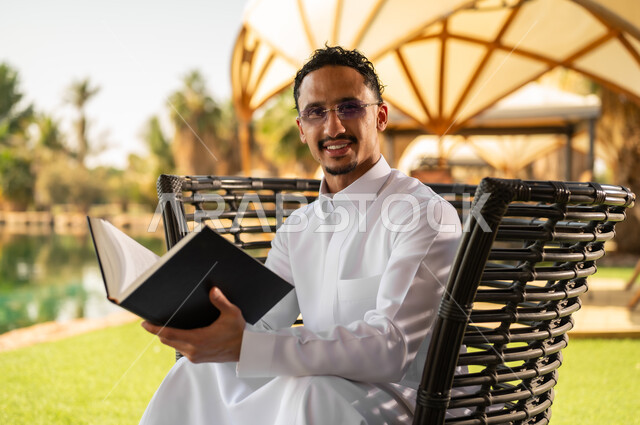 رجل سعودي بالثوب يقرأ كتاباً في الهواء الطلق