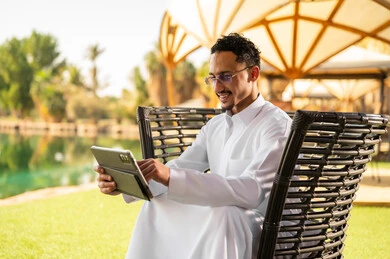 رجل سعودي بالثوب يستخدم جهاز لوحي في الحديقة
