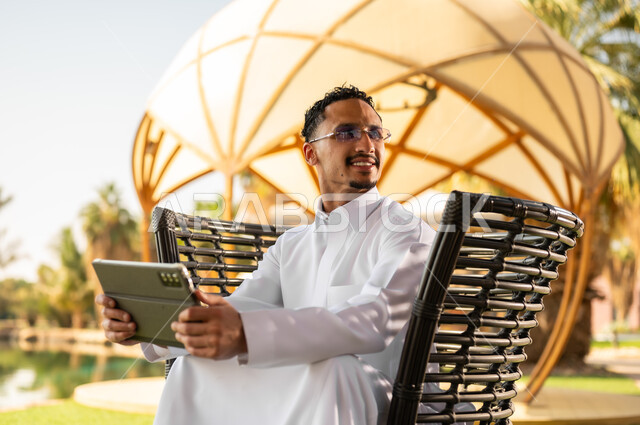 Saudi Man in Thobe Using Tablet in Outdoor Park