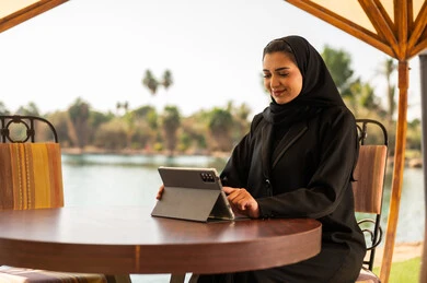 امرأة إماراتية بالعباءة تستخدم الجهاز اللوحي بالخارج