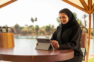 سيدة أعمال إماراتية تستخدم جهاز لوحي بجانب البحيرة