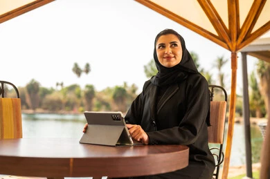 Saudi Woman Using Tablet at Outdoor Lakeside Cafe