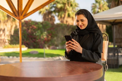 امرأة إماراتية بالعباءة تستخدم الهاتف الذكي في الخارج