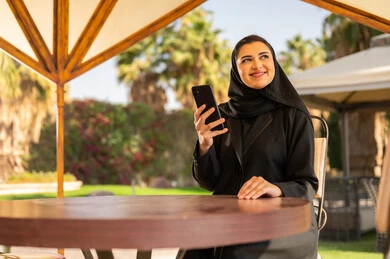 امرأة سعودية بالعباءة مع هاتف ذكي في مقهى خارجي