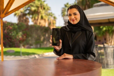 امرأة عربية تحمل هاتف ذكي بشاشة فارغة في الهواء الطلق