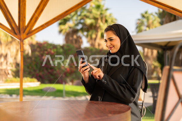 امرأة سعودية بالعباءة تستخدم الهاتف الذكي في الخارج
