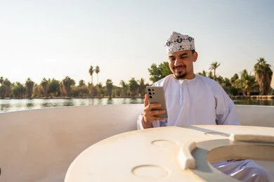 Omani Man in Traditional Dress Using Smartphone on Boat