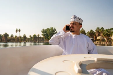 رجل عماني بالزي التقليدي يتحدث بالهاتف على متن قارب