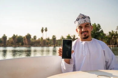 رجل عماني في قارب يمسك شاشة هاتف ذكي