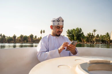 رجل عُماني يستخدم الهاتف الذكي على متن قارب