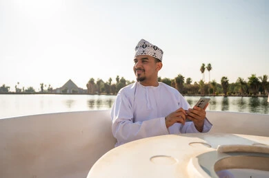 رجل عماني بهاتف ذكي على قارب بالقرب من البحيرة