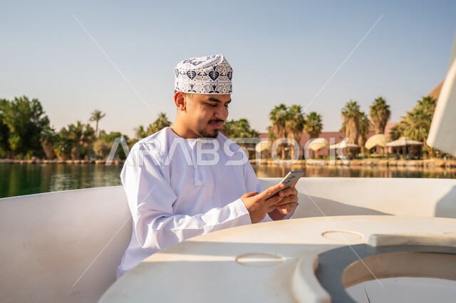 Omani Man in Traditional Dress Using Smartphone on Boat