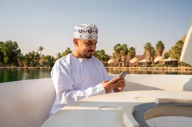 Omani Man in Traditional Dress Using Smartphone on Boat