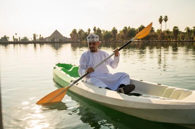 رجل عماني بالزي التقليدي يجدف في الكاياك عند الغروب