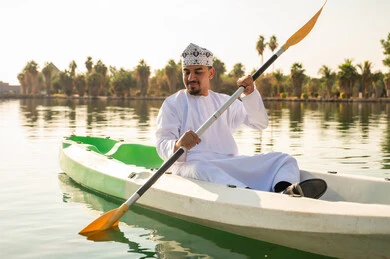 رجل عماني بالزي التقليدي يجدف في قارب الكاياك