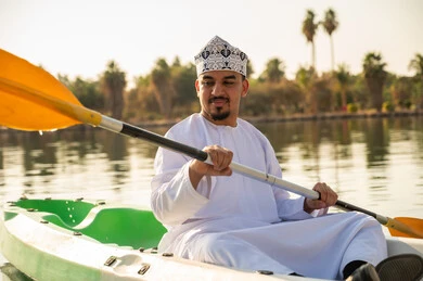 رجل عُماني يرتدي الكمة يجدف بقارب كاياك في بحيرة هادئة
