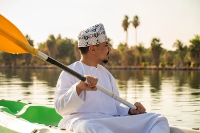 رجل عُماني بالزي التقليدي يجدف في قارب كاياك