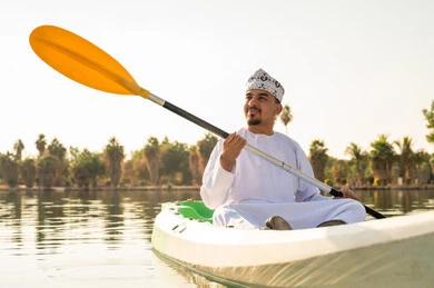 Omani Man Kayaking on Lake in Traditional Dress