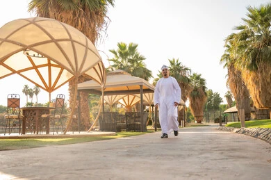 رجل عماني يمشي في حديقة منتجع مع مظلات
