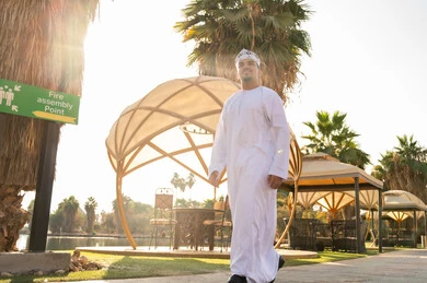 رجل عماني بالزي التقليدي في حديقة منتجع مشمسة