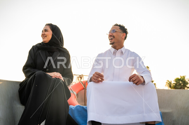 زوجان سعوديان يضحكان على متن قارب وقت الغروب
