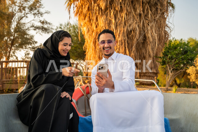 زوجان سعوديان على قارب يستخدمان الهاتف وقت الغروب