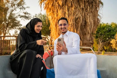 زوجان سعوديان على قارب يستخدمان الهاتف وقت الغروب