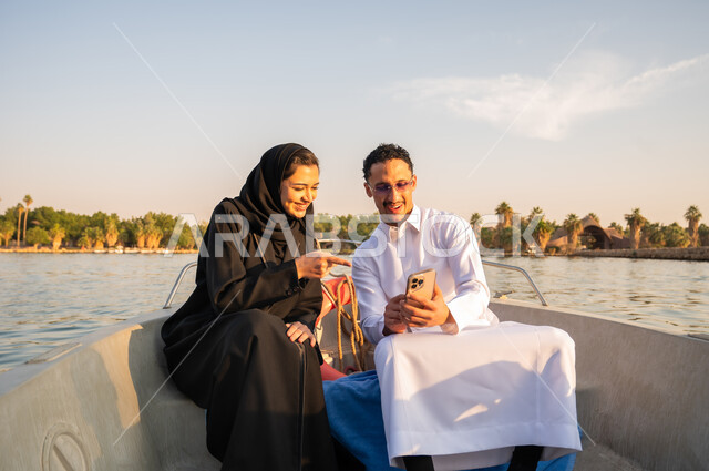 Saudi Couple Using Smartphone on Boat at Sunset