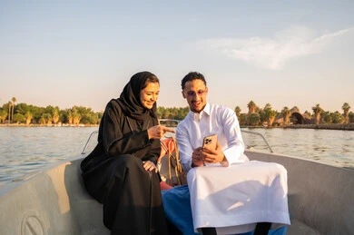 زوجان سعوديان يستخدمان الهاتف الذكي في قارب وقت الغروب