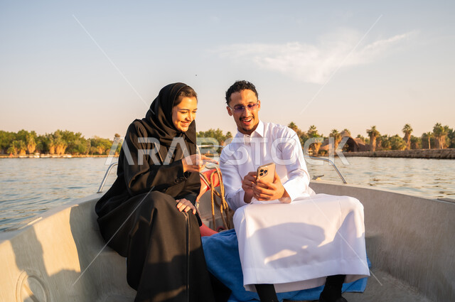 رجل وامرأة عربيان في قارب يستخدمان الهاتف وقت الغروب