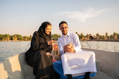 رجل وامرأة عربيان في قارب يستخدمان الهاتف وقت الغروب