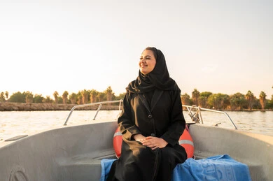 امرأة سعودية بالعباءة السوداء على متن قارب وقت الغروب