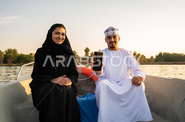 زوجان عمانيان على متن قارب مع هاتف ذكي وقت الغروب