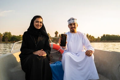 زوجان عمانيان على متن قارب مع هاتف ذكي وقت الغروب