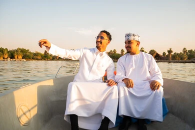 رجال عرب بالزي التقليدي في رحلة بحرية وقت الغروب