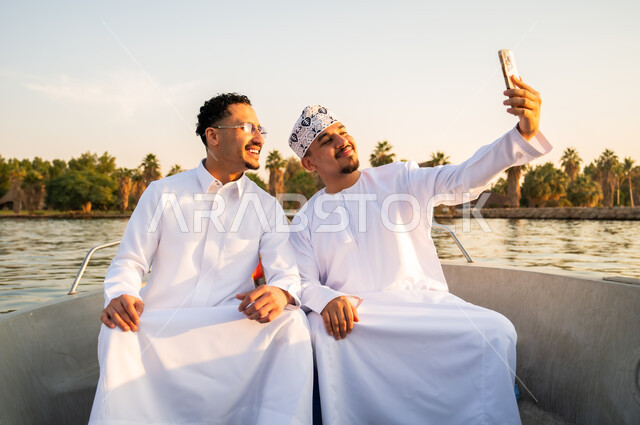 رجال عمانيون يلتقطون سيلفي على قارب وقت الغروب