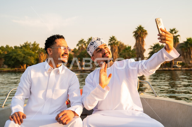 رجال عمانيون وعرب يلتقطون سيلفي على قارب وقت الغروب