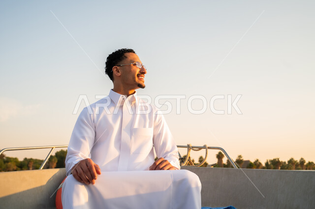 رجل سعودي بالثوب على متن قارب وقت الغروب