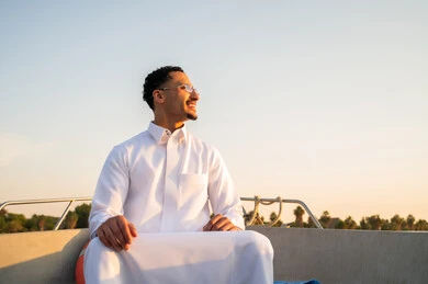 رجل سعودي بالثوب على متن قارب وقت الغروب