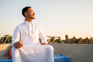 رجل سعودي يرتدي الثوب التقليدي على قارب وقت الغروب