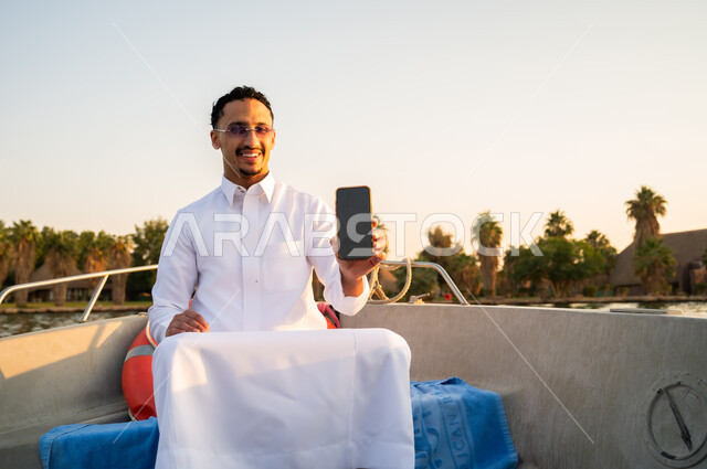 Saudi Man on Boat Holding Smartphone at Sunset